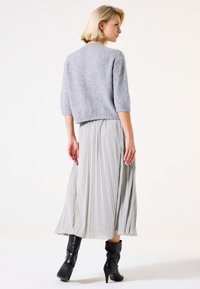 Pull en maille gris à manches courtes associé à une jupe midi plissée argentée. Bottines noires avec un léger talon.