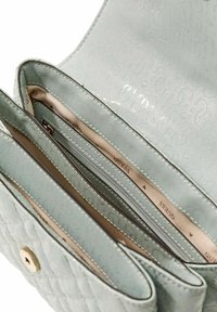 Sac à main matelassé vert clair avec une texture lisse. Comprend plusieurs compartiments et une poche zippée, ornés d'un motif de marque subtil.