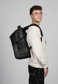 Mochila de cuadros en negro y gris con múltiples compartimentos y cremalleras, que cuenta con un respaldo acolchado y correas ajustables.