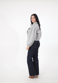 Grå, tekstureret, kort jakke med høj krave og puffede ærmer, kombineret med mørkeblå, vidde jeans og brune hæle.