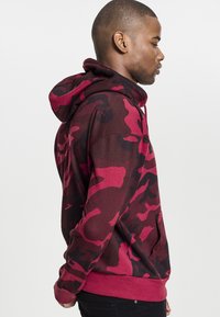 Felpa con cappuccio camouflage rossa e nera, in misto cotone, dotata di tasca a marsupio e polsini a coste. Presenta un cappuccio con cordino e una vestibilità comoda.