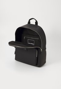 Black backpack made of smooth material, featuring a rounded shape, zip closure, front pocket, and interior compartments for organization.