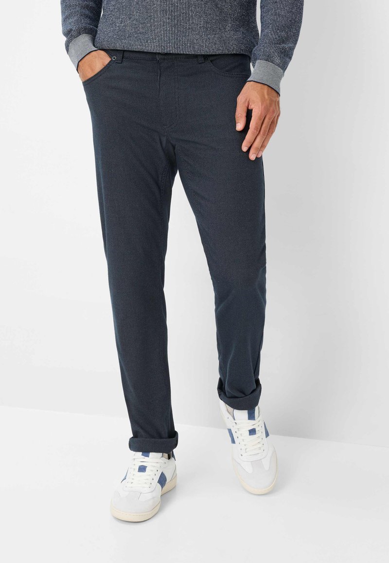 Donkerblauwe broek van gestructureerde stof, met een slim fit, zijzakken en een opgerolde zoom, gecombineerd met witte sneakers.