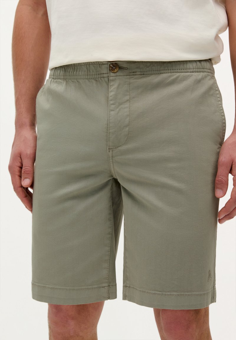 Shorts verts clairs avec une taille élastique et une fermeture à bouton, dotés de poches latérales et d'un ourlet droit. Fabriqués en tissu doux.