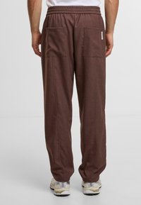 Bruine, losvallende broek van zacht materiaal met een elastische tailleband, met twee grote achterzakken en minimale naden.