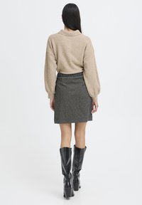 Lys beige strikket sweater med faldne skuldre, parret med en sort og hvid ternet miniskørt, og knæhøje sorte støvler.