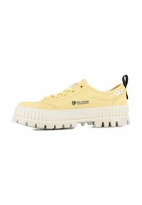 Zapatillas de lona amarillas con suela de goma blanca, fondo texturizado y logo prominente en el lateral. Cuenta con una lengüeta negra en el talón.