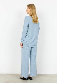 Luźny zestaw złożony z jasnoniebieskiego swetra i spodni, wykonany z miękkiej tkaniny o subtelnej fakturze. Całość uzupełniają czarne, płaskie buty.