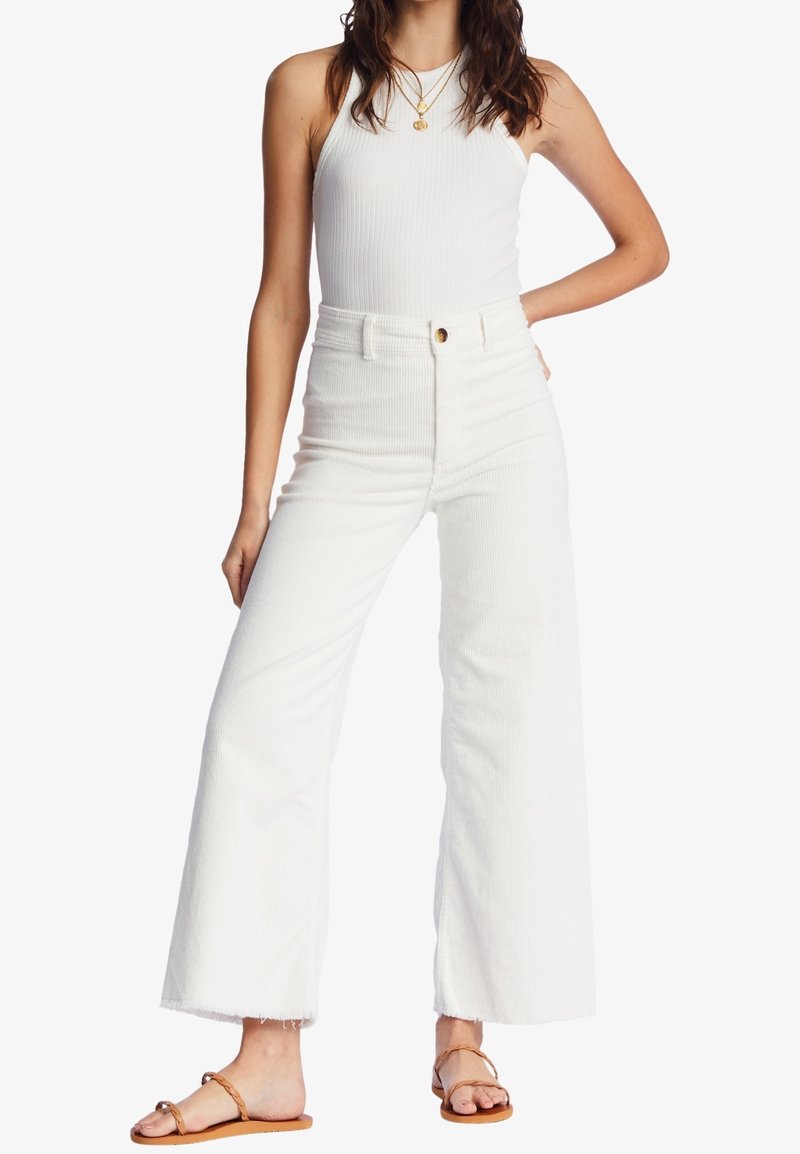 Vita ribbade högmidjade jeans med vida ben, med en framknappstängning och fransad kant. Matchas med en enkel vit linne.