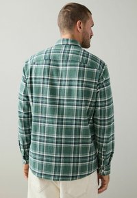 Green plaid flannel shirt with button closures, featuring a soft texture, a spread collar, and a curved hem. Back view shows distinct pattern.