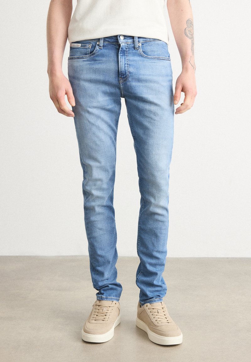 Jeans de mezclilla azul claro con corte slim, que cuentan con cinco bolsillos y un cierre de botón. Combinados con zapatillas beige.