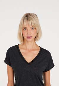 T-shirt nera a V con maniche corte arrotolate, realizzata in un morbido tessuto e con un sottile bordo in rete attorno al collo per un tocco di texture.