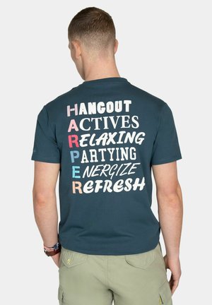 Hombre con camiseta verde oscuro con las palabras «HANGOUT, ACTIVES, RELAXING, PARTYING, ENERGIZE, REFRESH» en letras de colores en la parte trasera.