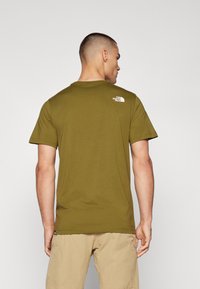 Oliven grønn kortermet t-skjorte laget av myk stoff. Har en liten hvit logo på øvre del av ryggen. Standard rund hals-designe.
