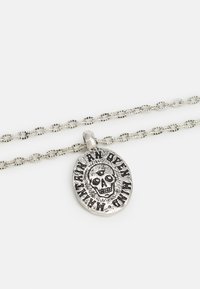 Colar de prata com uma corrente de duas camadas, apresentando um pendente oval gravado com um crânio e o texto "Uma Mente Aberta". Superfície texturizada.