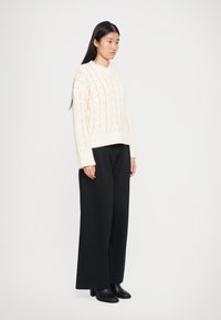 Pull en maille crème avec un motif en chevrons, associé à un pantalon large taille haute noir et des bottines à talons noires.