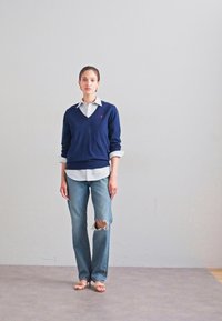Navy blue sweater over a white striped shirt, paired with faded ripped jeans and beige sandals. Simple design with a relaxed fit.
