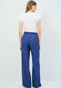 Top ligero de mangas cortas blancas combinado con pantalones de encaje azules que presentan patrones intrincados y una cinturilla estructurada, con pierna acampanada.