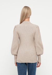 Beige ribbestrikket genser med puffermer, slim fit, rund hals og teksturert strikk. iført over blå denimjeans, vist fra baksiden.