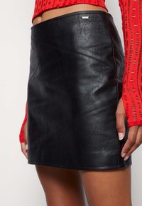 Mustan nahkaisen minihameen tekstuuri on hieno, kulmikkaat sauman yksityiskohdat ja tyylikäs siluetti. Kiinnitetty vähäisellä metallilla.