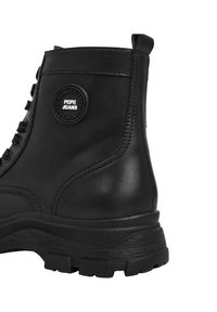 Bota de tobillo de cuero negro con un logo redondo de Pepe Jeans, suela de goma texturizada y detalles cosidos en la parte superior.