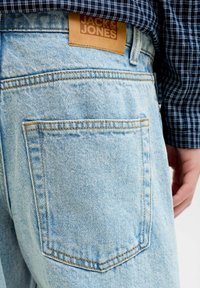 Világos kék farmernadrág hátul zsebbel, barna bőr címkével, amelyen a "JACK & JONES" felirat olvasható. Az anyag kopott, texturált megjelenésű.