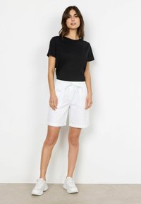 Black short-sleeve t-shirt paired with white shorts featuring an elastic waistband and drawstring. Model wearing white athletic shoes.