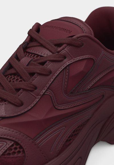 Μπορντό αθλητικό παπούτσι με κορδόνια, χαρακτηριστικά από υφή, λεπτομέρειες από διχτυωτό ύφασμα και ανάγλυφο λογότυπο Emporio Armani στη γλώσσα.
