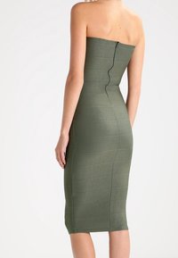 Figurbetontes, trägerloses Midi-Kleid in Olivgrün mit horizontalen Liniendetails und einem Reißverschluss auf der Rückseite. Hergestellt aus glattem, elastischem Material.