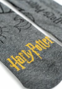 Calze grigie con illustrazioni stampate nere e testo "Harry Potter" giallo in un font audace e stilizzato. Tessuto in maglia morbida.