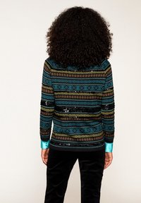 Długi sweter z długim rękawem w kolorze niebieskim, brązowym i złotym z geometrycznymi wzorami oraz akcentami z cekinów. Oferuje jednolitą turkusową mankietę i dół.