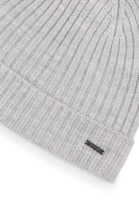 Lichtgrijze gebreide muts met een geribbelde structuur, omgeslagen boord en een klein metalen logolabel aan de zijkant. Zachte textuur en warm materiaal.