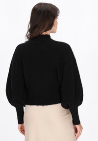 Maglione nero corto con colletto alto, maniche a sbuffo oversize e finitura lavorata a maglia. Dettaglio con orlo sfilacciato nella parte inferiore.
