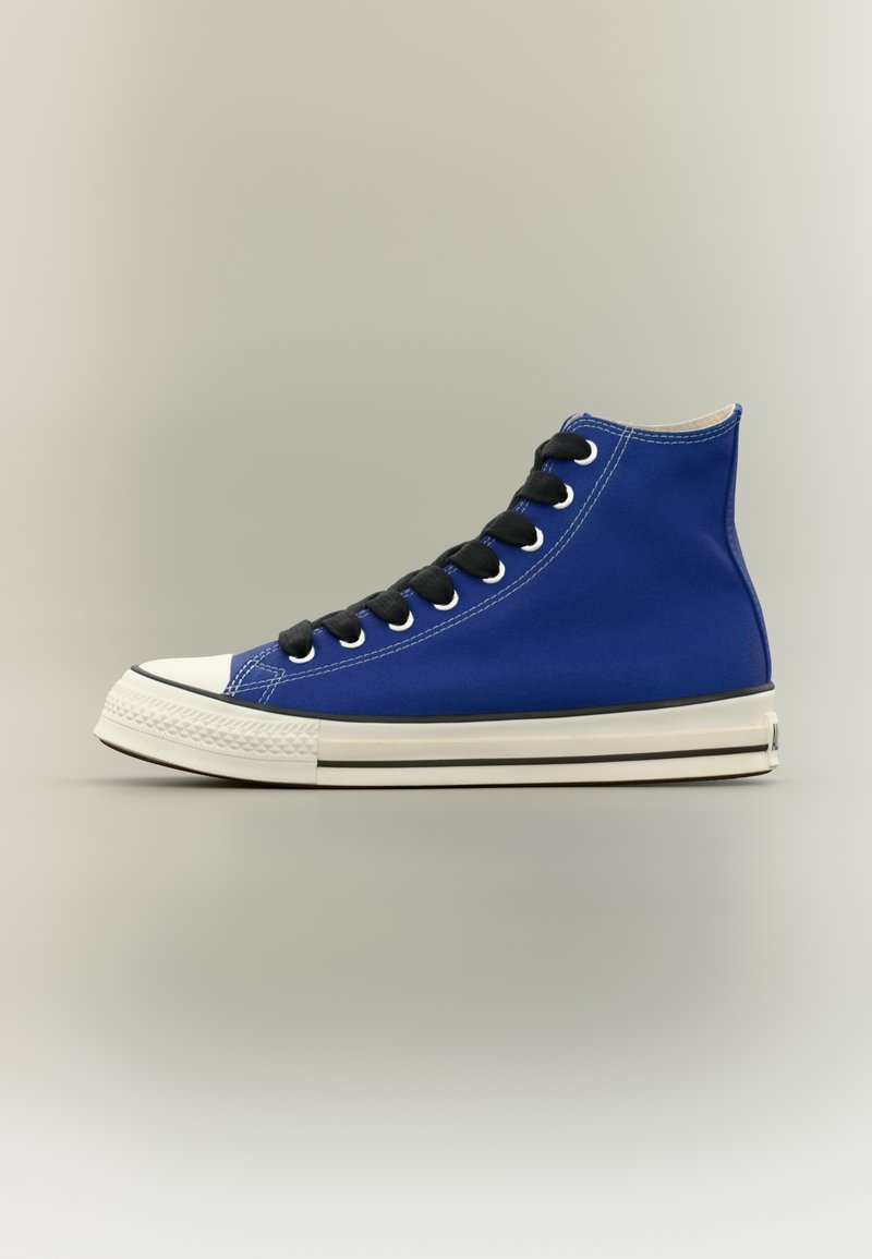 Μπλε ψηλό αθλητικό παπούτσι με μαύρα κορδόνια, λευκή λαστιχένια μύτη και εκρού σόλα με μαύρη ρίγα, εμφανίζεται από το πλάι σε ουδέτερο φόντο.