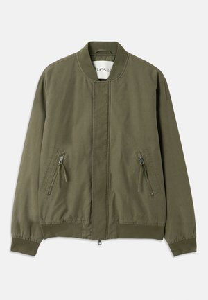 Olive green bomber jacket with a round neck, two zippered front pockets, elastic cuffs, and a clean, minimalist design. Casual fabric texture.