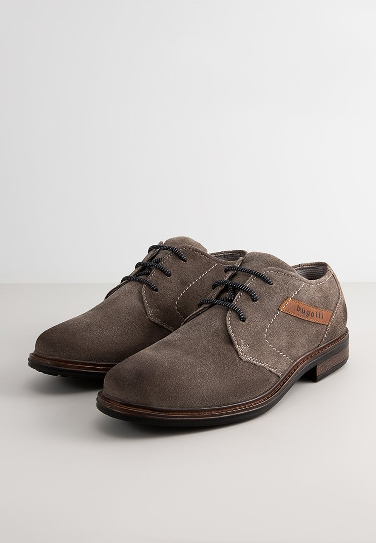 Zapatos de vestir de ante marrón con textura suave, costuras blancas, cordones negros y un parche de cuero marrón con el nombre de la marca.