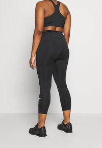 Black athletic leggings and a matching bra, fitted design with a smooth texture. Notable Nike logo on the leg and sleek styling.