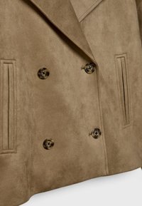 Veste croisée en daim marron clair avec quatre boutons en écaille et deux poches passepoilées verticales.