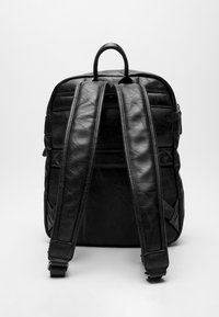 Mochila de cuero negro con correas acolchadas, textura suave, parte superior redondeada y compartimentos con cremallera. Diseño minimalista sin logotipos visibles.