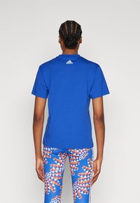 Kungsblå kortärmad t-shirt med rund halsringning, med vit Adidas-logga på baksidan; matchad med mönstrade leggings med blå, röda och vita detaljer.