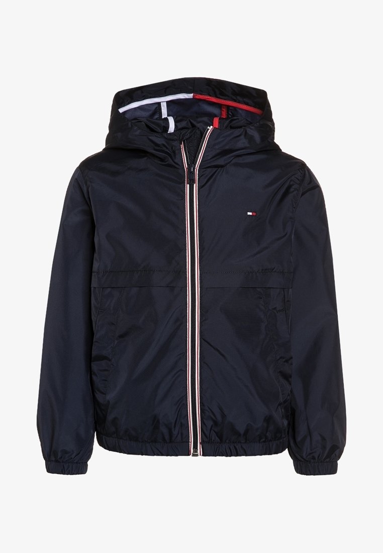 Tummansininen huppupuvuntakki, jossa on vetoketjukiinnitys, joustavat hihansuut ja punaiset sekä valkoiset korosteteipit vetoketjun vieressä.