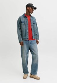 Denim jope kahe eesmine taskutega, punane T-särk all, helesinised teksad ja beežid mokasisad, koos musta mütsiga.