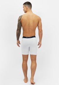 Vita boxertrosor med ett marinblått midjeband som har en logotyp, åtsittande design, slät textur och en längd som når mitt på låret.