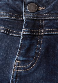 Mörkblå denimjeans med en metallknapp med "BY STREET ONE" inristad, synlig sömnad och en slät yta. Designade med klassiska fickor.