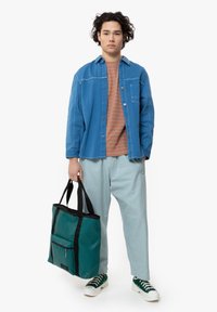 Camicia di denim blu, t-shirt a righe arancioni, pantaloni blu chiaro, borsa a tracolla verde con dettagli neri, sneakers bianche con particolari verdi.