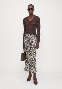 Brown lace long-sleeve top with scalloped neckline, paired with a high-waisted white skirt featuring a black abstract pattern. Burgundy heels and green bag.