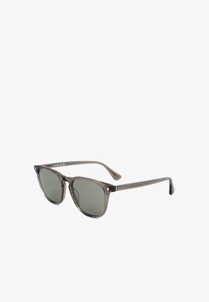 Occhiali da sole con montatura in plastica grigia trasparente, lenti tondeggianti quadrate con tintura scura e aste sottili e dritte.