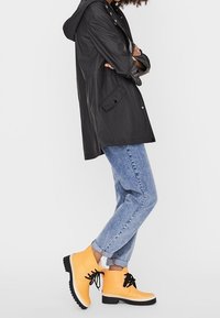 Czarna wodoodporna kurtka z kapturem, zestawiona z jasnoniebieskimi dżinsami i jaskrawozłotymi butami z czarnymi sznurowadłami oraz białą podeszwą.