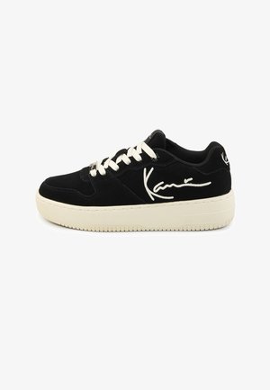 Pantof sport negru cu glezna joasă, talpă groasă albă, șireturi albe și semnătură stilizată albă pe lateral și pe călcâi.