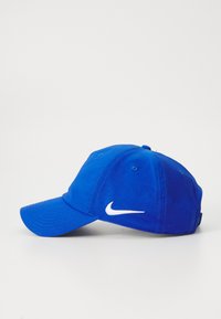 Blå baseballcaps laget av bomull med buet skjerm, med en hvit Nike-logo på siden og seks ventilasjonsøyler på toppen.